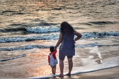 Rear view of mother with daughter standing at beach during sunset