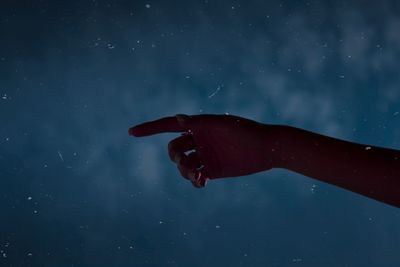 Cropped hand of woman gesturing against sky at night