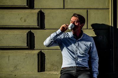 Man drinking coffee while leaning on wall