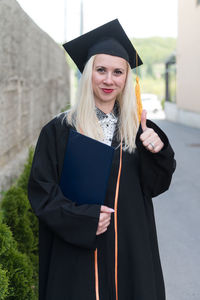 Portrait of woman wearing graduation gown standing against trees