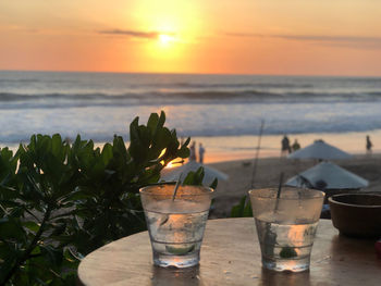 Close-up of drink on table against sea during sunset