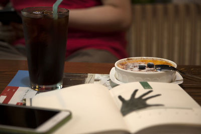 Close-up of drink and creme brulee on table with woman sitting in background