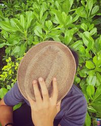 Close-up of man holding hat sitting by plants