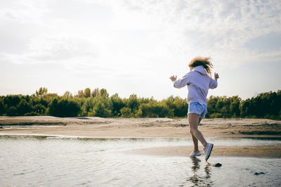 Rear view of woman balancing on rocks at beach against sky