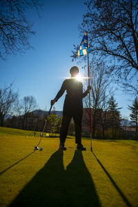 Golfer on the putting green and holding the golf flag and golf putter with sunlight.