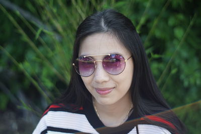 Close-up portrait of smiling young woman wearing sunglasses against plant