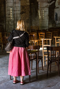 Rear view of woman standing by chairs on floor in church 