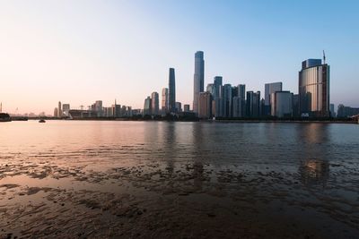 Sea by modern buildings against clear sky