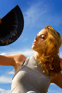 Low angle view of young woman with hand fan against sky during sunny day