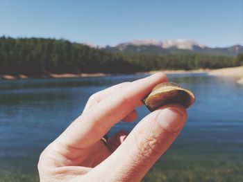 Close-up of hand holding snail against sky