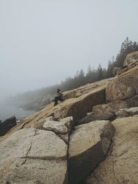 Man sitting on rock against sky