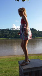 Side view full length of girl standing on retaining wall against lake