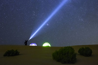 Man with flashlight standing on landscape against sky at night