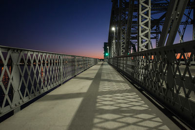 Empty walkway on bridge against sky during sunset