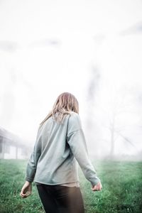 Rear view of man walking on field against sky