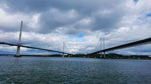 Suspension bridge over river against cloudy sky