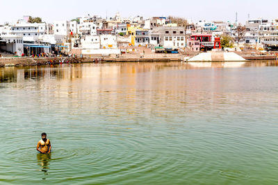 Man in river against buildings in city