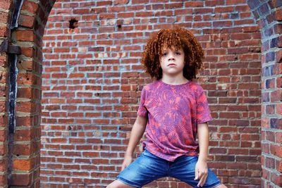 Portrait of boy standing with legs apart against brick wall