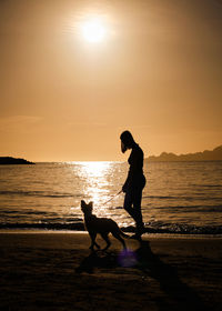 Silhouette woman standing at beach against sky during sunset