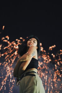 Portrait of young woman posing while standing against firework display