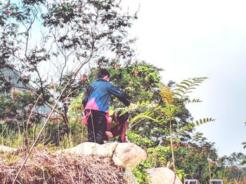 Man sitting by tree against sky