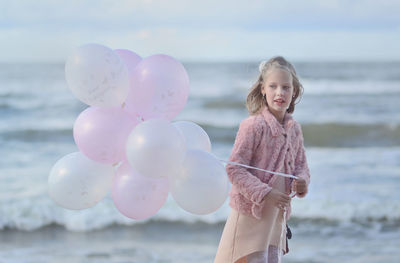 Girl holding balloon while standing against sea at beach