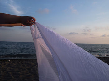 Midsection of person by sea against sky during sunset