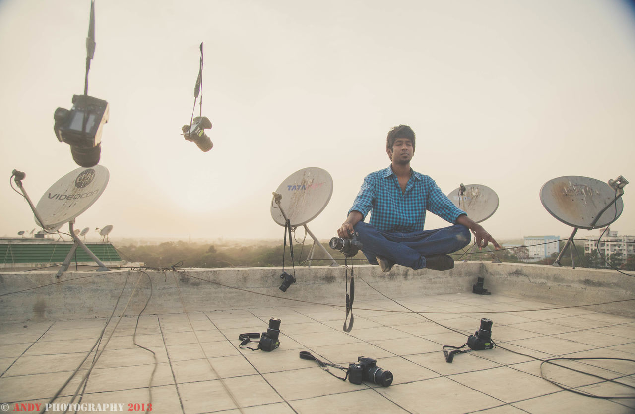 YOUNG MAN SITTING ON SEAT AGAINST SKY