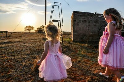 Cute sisters walking on field against sky during sunset