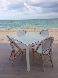 Deck chairs on table by sea against sky