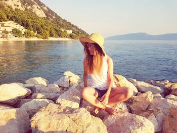 Woman sitting on rock by sea against sky