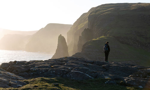 Silhouette man standing on land by sea against sky during sunset