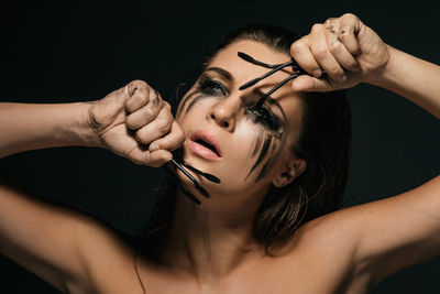 Portrait of young woman holding mascara against black background