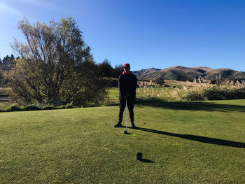 View of man about to tee off on a golf course against clear sky