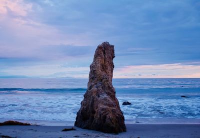 Rock formation on beach against sky during sunset