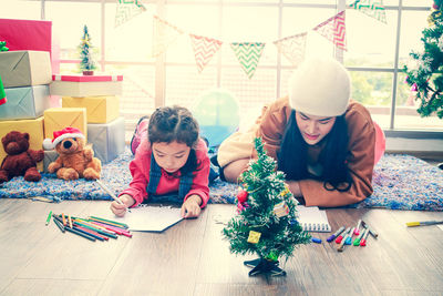 Rear view of girl and christmas tree on floor at home