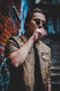 Close-up of man in sunglasses smoking cigarette against wall