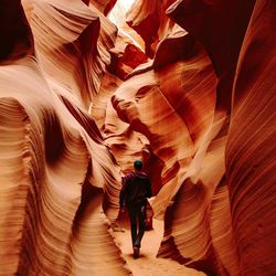 Rear view of man walking amidst sandstones at antelope canyon