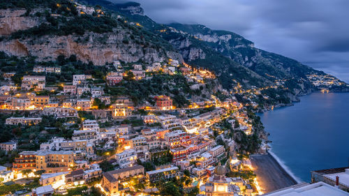 High angle view of illuminated buildings by sea against sky