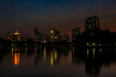 Illuminated buildings by river against sky at night