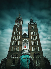 Rear view of mid adult woman with backpack looking at church while standing against cloudy sky