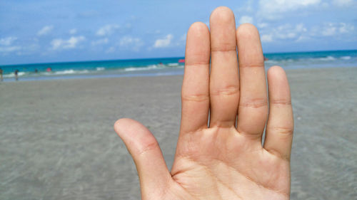 Close-up of cropped hand at beach against cloudy sky