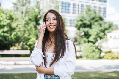 Portrait of young asian woman student with long hair using mobile phone in city park