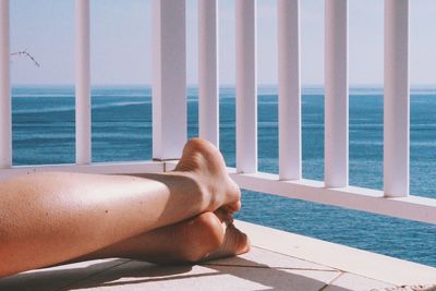 Low section of woman relaxing by railing against sea