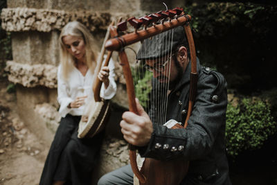 Male and female playing lyra instrument in public park