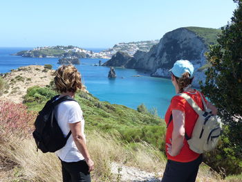 Rear view of women standing on rock by sea against clear sky