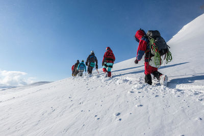 Low angle view of people on snowcapped mountain against sky