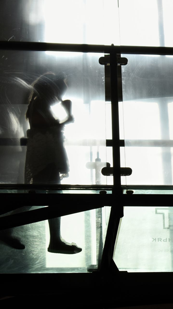 REAR VIEW OF WOMAN LOOKING THROUGH WINDOW AT HOME