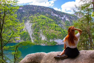 Woman sitting on rock by lake against mountains