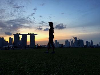 Silhouette of woman standing on park bench in city at dusk